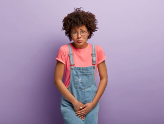 a young woman with brown hair dressed in a bright pink shirt and blue denim dungarees.