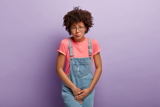 a young woman with brown hair dressed in a bright pink shirt and blue denim dungarees.